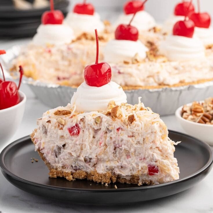 Slice of millionaire pie with creamy fruit and nut filling, topped with whipped cream and a cherry.