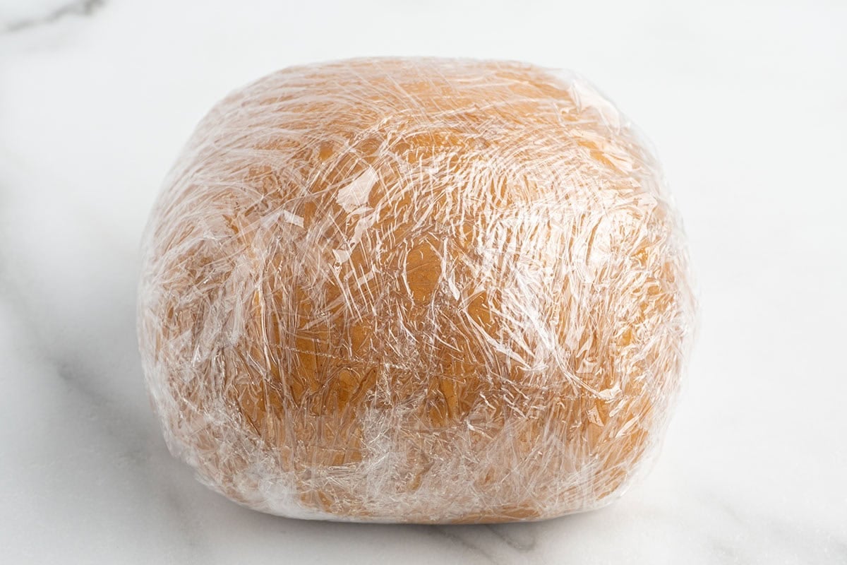 Peanut butter cheese ball mixture shaped into a ball and wrapped in plastic wrap to chill.