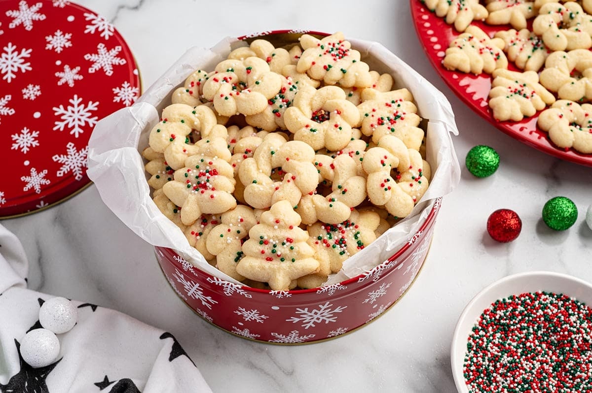 Spritz cookies in a red snowflake tin with green and red sprinkles.