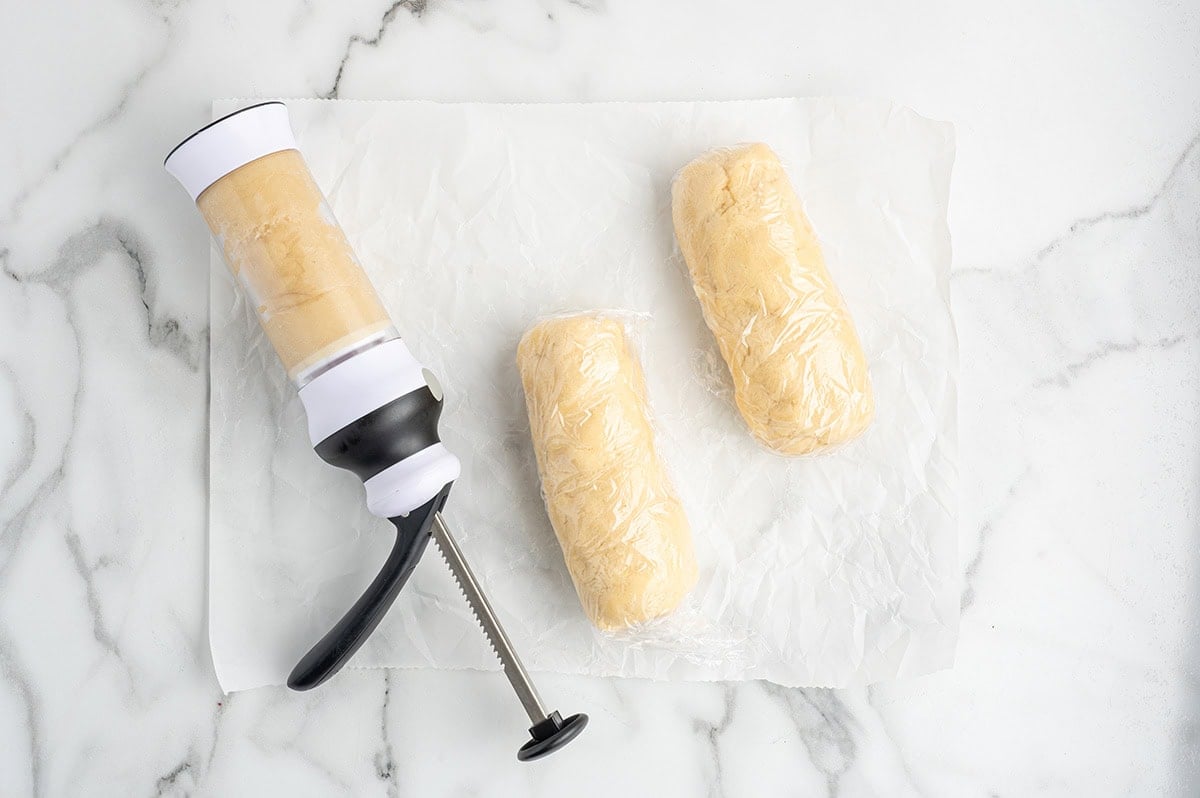 Cookie dough wrapped in plastic next to a cookie press loaded with dough.