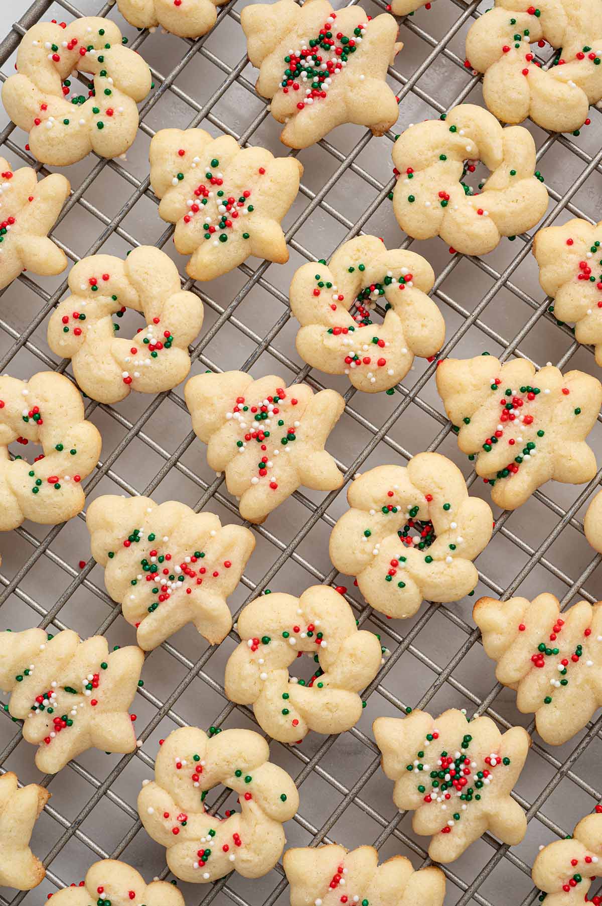 Spritz cookies shaped like wreaths and trees with holiday sprinkles on a wire cooling rack.