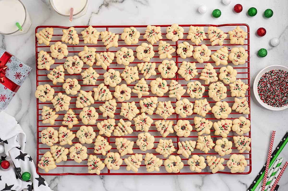 Spritz cookies in assorted shapes with holiday sprinkles on a red cooling rack.